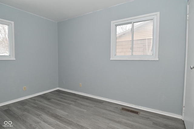 unfurnished room with dark wood-type flooring, visible vents, and baseboards