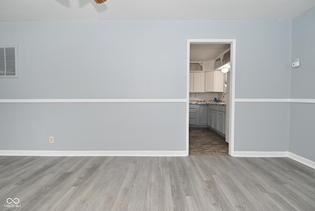 unfurnished room with a sink, wood finished floors, visible vents, and baseboards