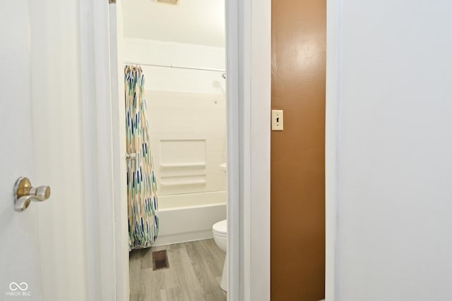 bathroom with toilet, shower / bathtub combination with curtain, and hardwood / wood-style floors