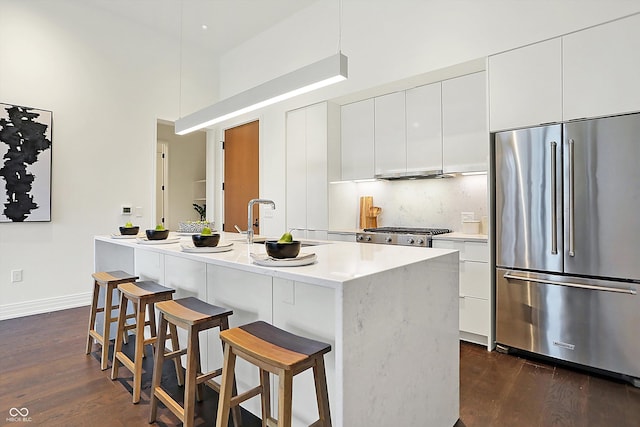 kitchen with white cabinets, dark hardwood / wood-style floors, stainless steel built in fridge, and a center island with sink