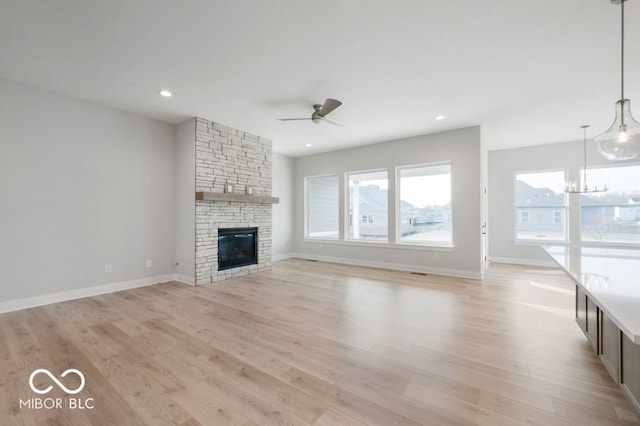 unfurnished living room featuring a fireplace, ceiling fan with notable chandelier, and light hardwood / wood-style flooring