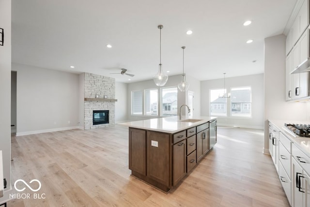 kitchen with sink, a fireplace, white cabinets, a center island with sink, and light wood-type flooring