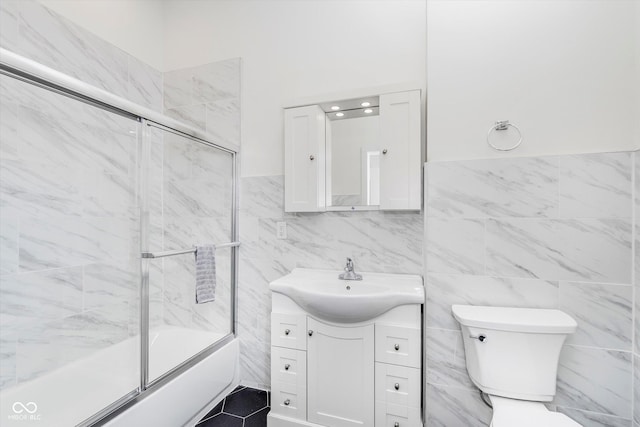 full bathroom featuring toilet, vanity, shower / bath combination with glass door, and tile walls