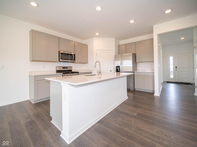 kitchen with dark wood-type flooring, gray cabinets, an island with sink, and appliances with stainless steel finishes