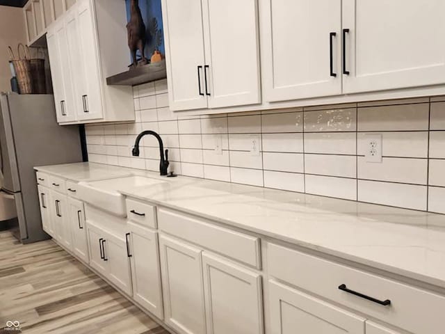 kitchen featuring white cabinetry, sink, stainless steel fridge, and light stone countertops