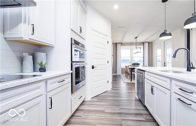 kitchen with white cabinets, hanging light fixtures, range hood, and appliances with stainless steel finishes