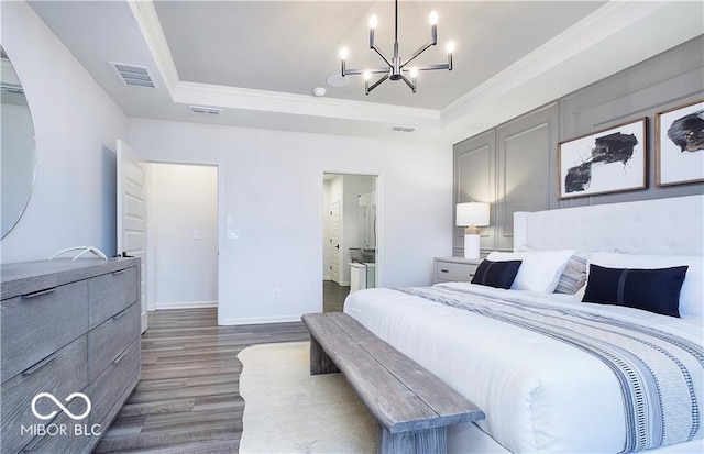 bedroom with ensuite bathroom, ornamental molding, a tray ceiling, and dark wood-type flooring