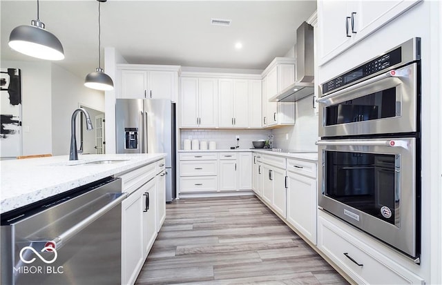 kitchen featuring stainless steel appliances, light stone counters, wall chimney exhaust hood, white cabinets, and tasteful backsplash