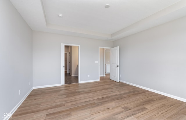 unfurnished bedroom featuring a raised ceiling and light wood-type flooring