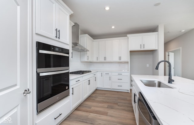 kitchen with sink, stainless steel appliances, white cabinets, and wall chimney range hood