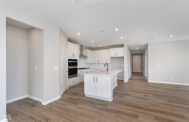 kitchen featuring an island with sink, stainless steel gas cooktop, dark hardwood / wood-style flooring, wall chimney exhaust hood, and white cabinets