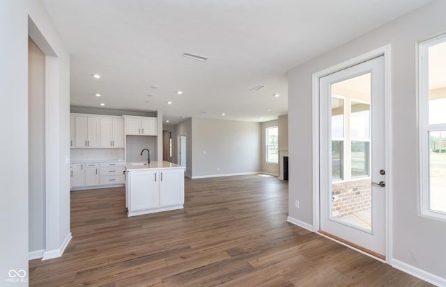 kitchen with white cabinets, dark wood-type flooring, a kitchen island with sink, and sink