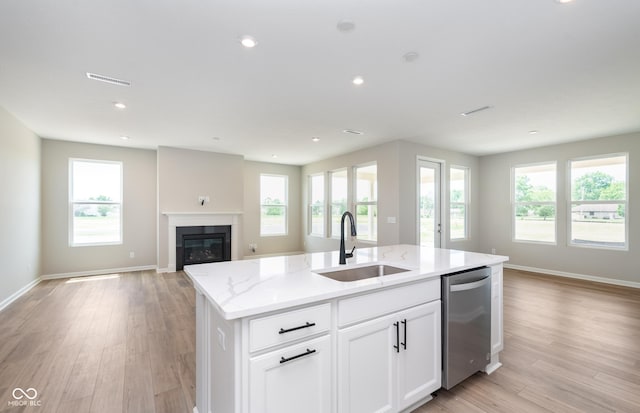 kitchen featuring white cabinets, a kitchen island with sink, light stone counters, sink, and stainless steel dishwasher