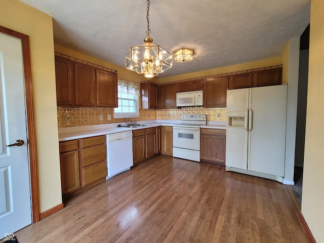 kitchen with a textured ceiling, white appliances, sink, light hardwood / wood-style floors, and hanging light fixtures