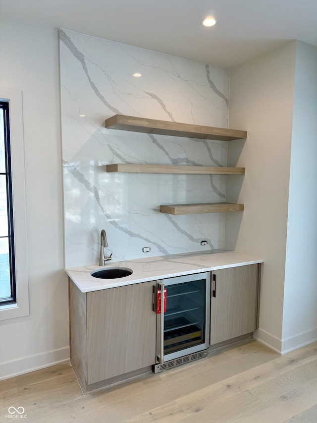 bar featuring sink, decorative backsplash, beverage cooler, and light wood-type flooring