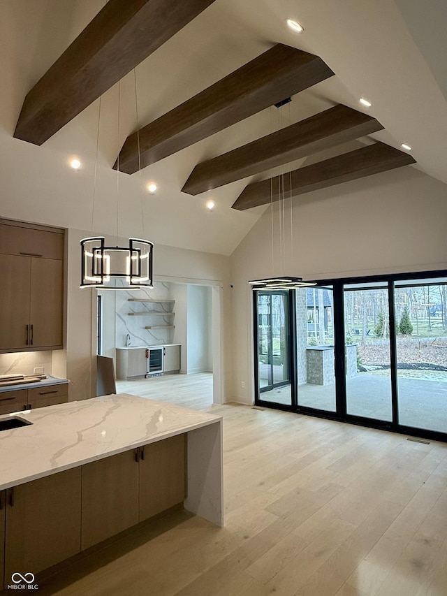 kitchen with high vaulted ceiling, hanging light fixtures, light wood-type flooring, beam ceiling, and light stone countertops