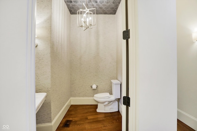 bathroom with toilet, hardwood / wood-style floors, and an inviting chandelier