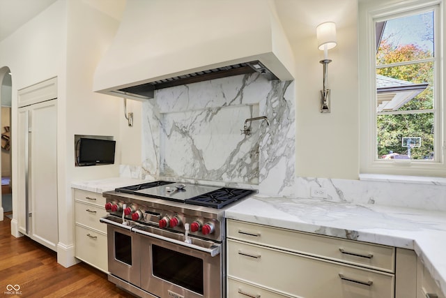 kitchen featuring range with two ovens, dark hardwood / wood-style flooring, light stone counters, backsplash, and premium range hood