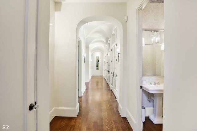 corridor featuring dark wood-type flooring, an inviting chandelier, and sink