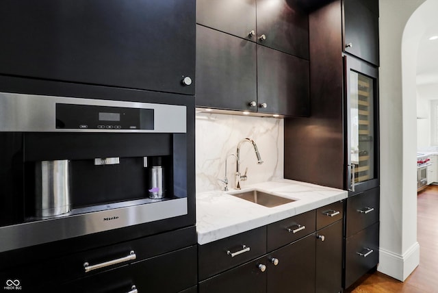 kitchen featuring light stone counters, sink, tasteful backsplash, stainless steel oven, and light hardwood / wood-style floors