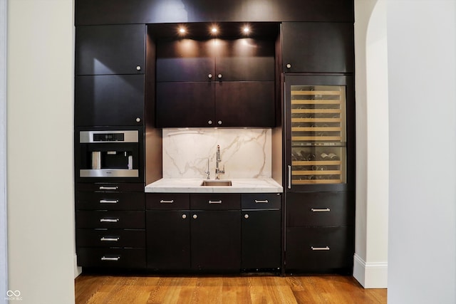 bar featuring stainless steel oven, wine cooler, light hardwood / wood-style flooring, and sink