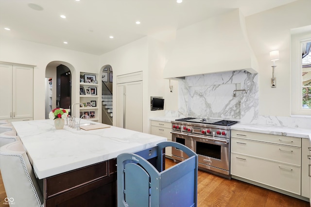 kitchen featuring light stone countertops, luxury range, hardwood / wood-style flooring, sink, and a center island with sink