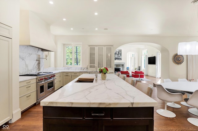 kitchen featuring range with two ovens, tasteful backsplash, dark hardwood / wood-style flooring, sink, and a kitchen bar