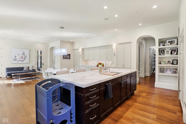 kitchen featuring light hardwood / wood-style flooring, decorative light fixtures, sink, an island with sink, and white cabinets