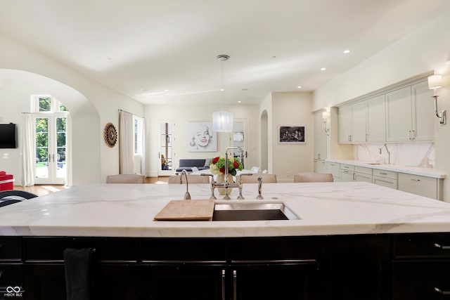 kitchen with light stone counters, sink, decorative light fixtures, a center island with sink, and backsplash