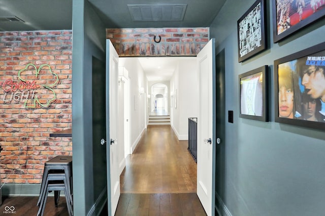 corridor with brick wall and dark hardwood / wood-style flooring