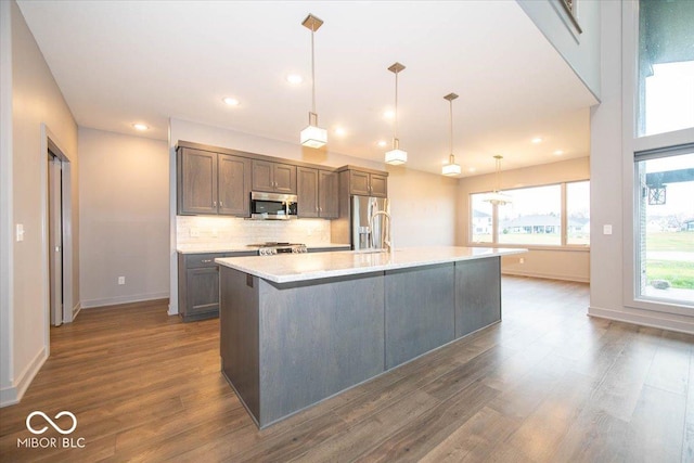 kitchen with stainless steel appliances, dark hardwood / wood-style floors, backsplash, decorative light fixtures, and a kitchen island with sink