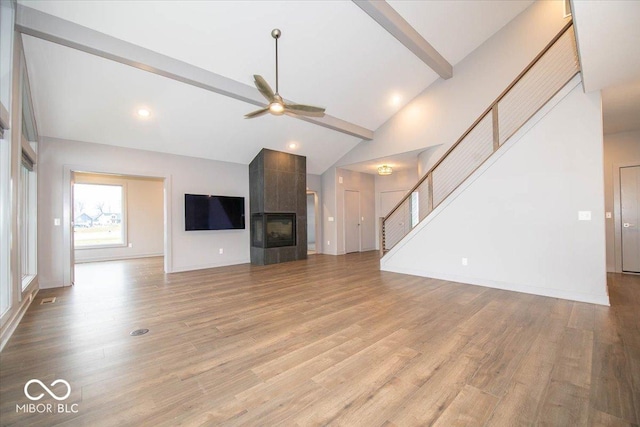 unfurnished living room featuring a tile fireplace, high vaulted ceiling, light hardwood / wood-style flooring, ceiling fan, and beam ceiling