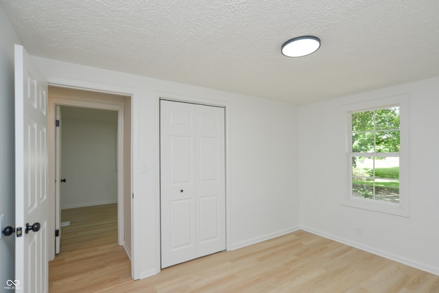 unfurnished bedroom featuring light hardwood / wood-style floors, a textured ceiling, and a closet