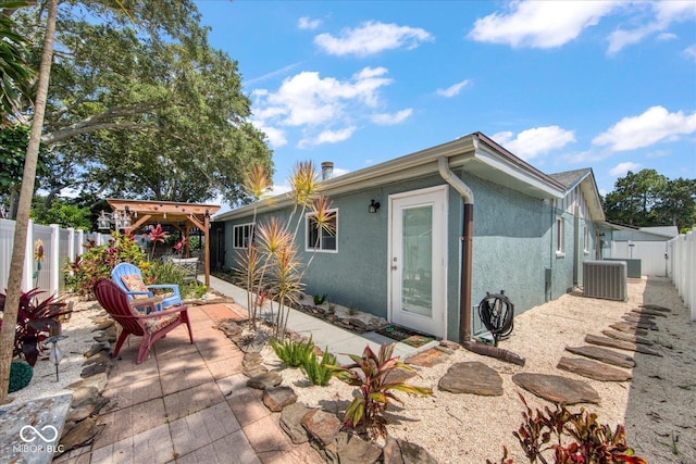 rear view of property featuring a patio, central AC unit, a fenced backyard, and stucco siding