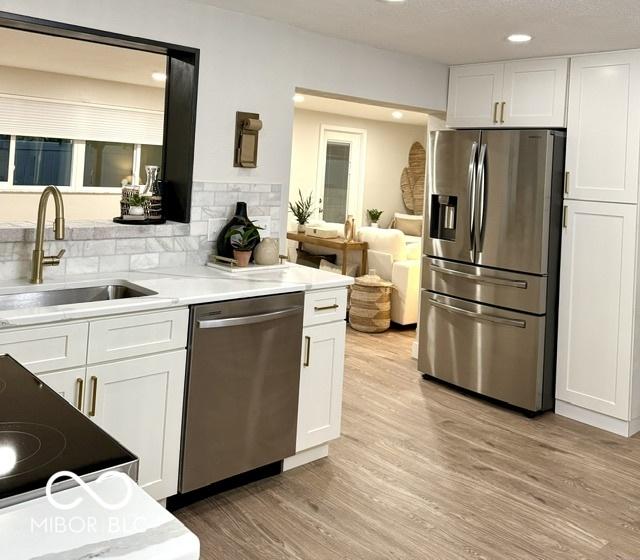 kitchen with light wood finished floors, a sink, white cabinets, appliances with stainless steel finishes, and backsplash