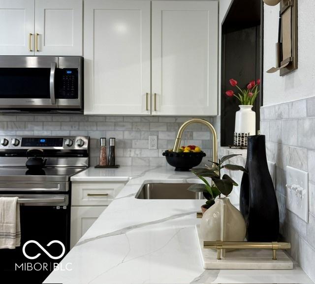 kitchen with light stone countertops, decorative backsplash, appliances with stainless steel finishes, white cabinets, and a sink