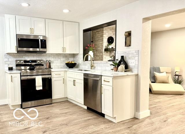 kitchen featuring a sink, stainless steel appliances, light countertops, white cabinets, and light wood-style floors