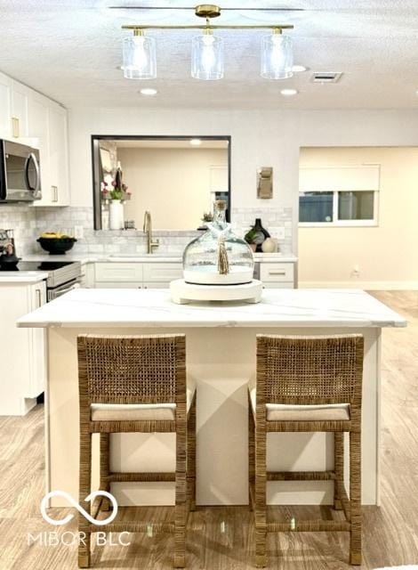 bar featuring tasteful backsplash, stainless steel microwave, visible vents, a textured ceiling, and a sink