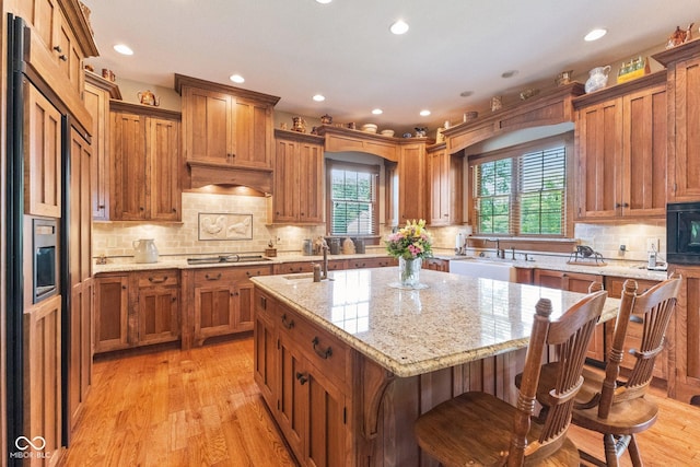 kitchen featuring sink, light hardwood / wood-style flooring, an island with sink, a breakfast bar area, and light stone counters