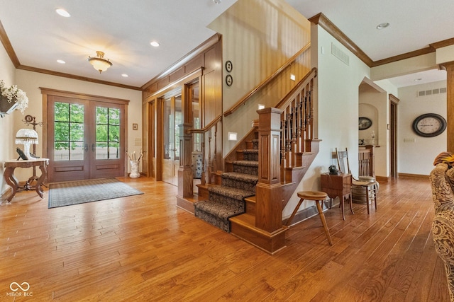 entrance foyer with ornamental molding, light hardwood / wood-style floors, and french doors