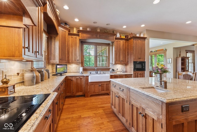 kitchen featuring a kitchen island, black appliances, sink, light hardwood / wood-style flooring, and light stone countertops