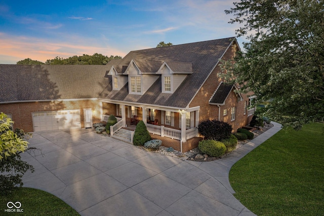 new england style home featuring a lawn, covered porch, and a garage