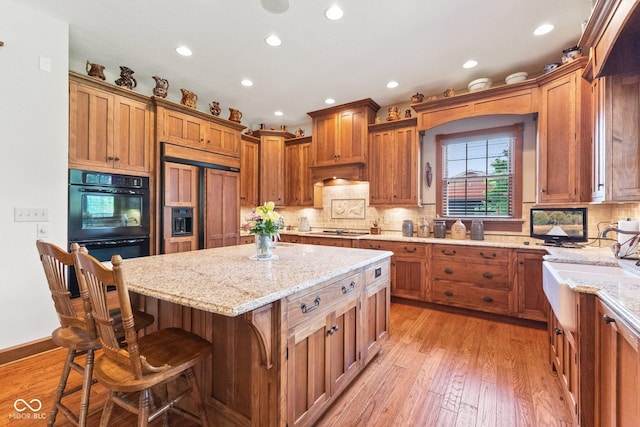 kitchen with paneled refrigerator, a kitchen breakfast bar, light wood-type flooring, light stone counters, and a center island