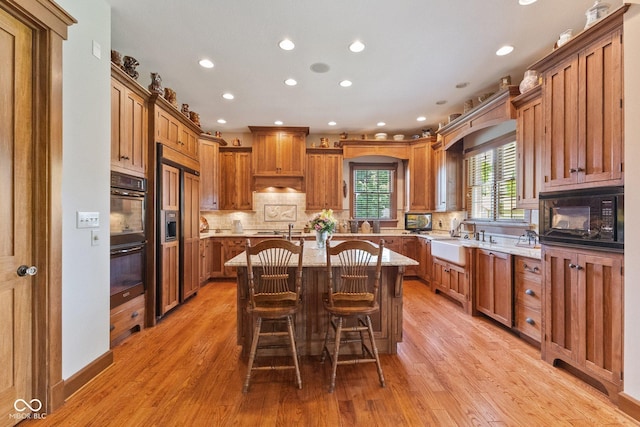 kitchen with black appliances, a kitchen island, a kitchen bar, sink, and light wood-type flooring