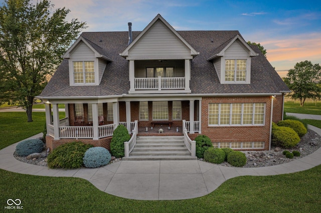 view of front of property with covered porch, a lawn, and a balcony