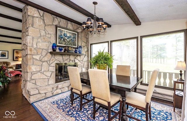 dining space featuring dark wood-type flooring, a stone fireplace, a chandelier, a textured ceiling, and beamed ceiling