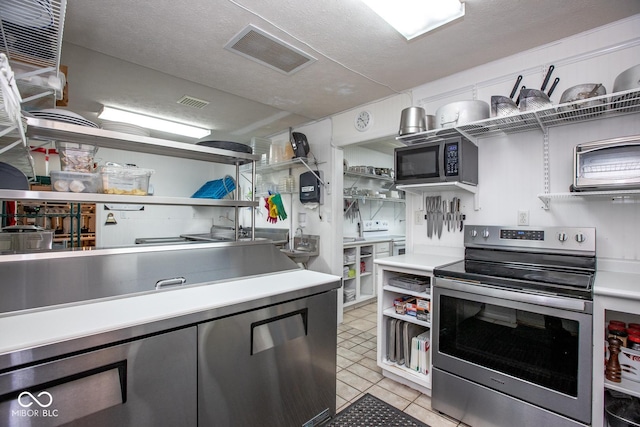 kitchen featuring light tile patterned flooring, stainless steel range with electric cooktop, and a textured ceiling