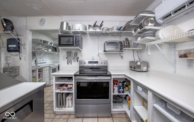 kitchen with light tile patterned flooring, stainless steel range with electric stovetop, sink, and white range with electric cooktop