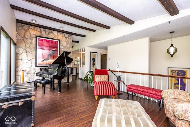 living area featuring plenty of natural light, dark wood-type flooring, a textured ceiling, and beam ceiling