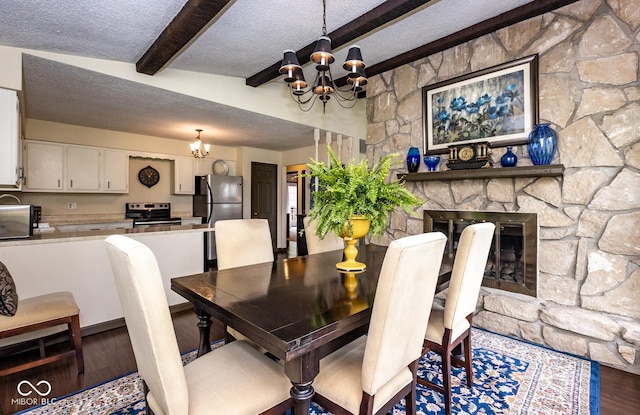 dining space featuring hardwood / wood-style floors, lofted ceiling with beams, a textured ceiling, a stone fireplace, and a chandelier